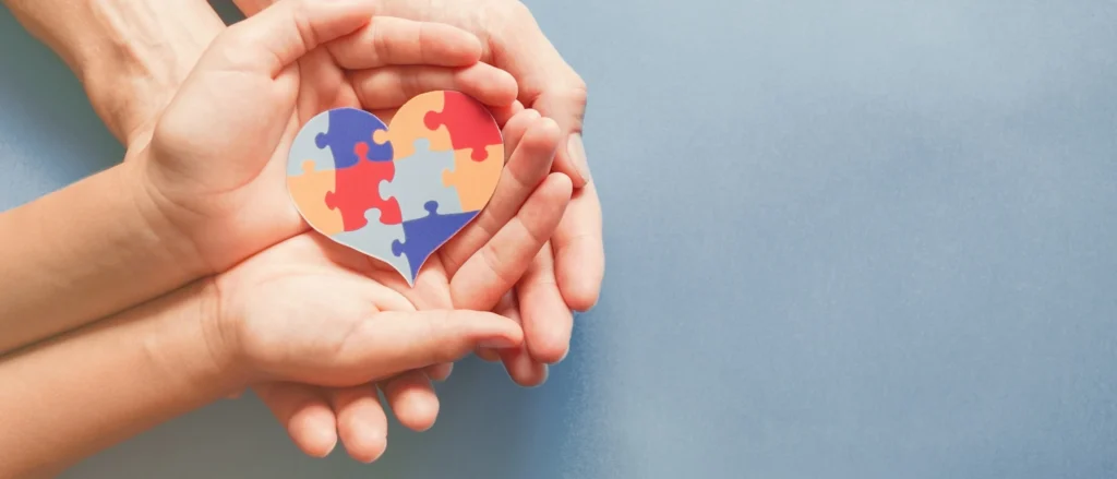 A pair of hands with a heart shaped jigsaw resting on top of them. This pair of hands is, in turn, resting on top of another pair of hands.