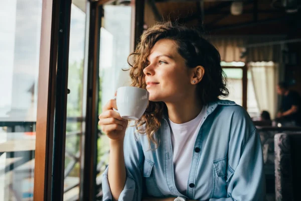 Young women looking out the window with a hot drink.